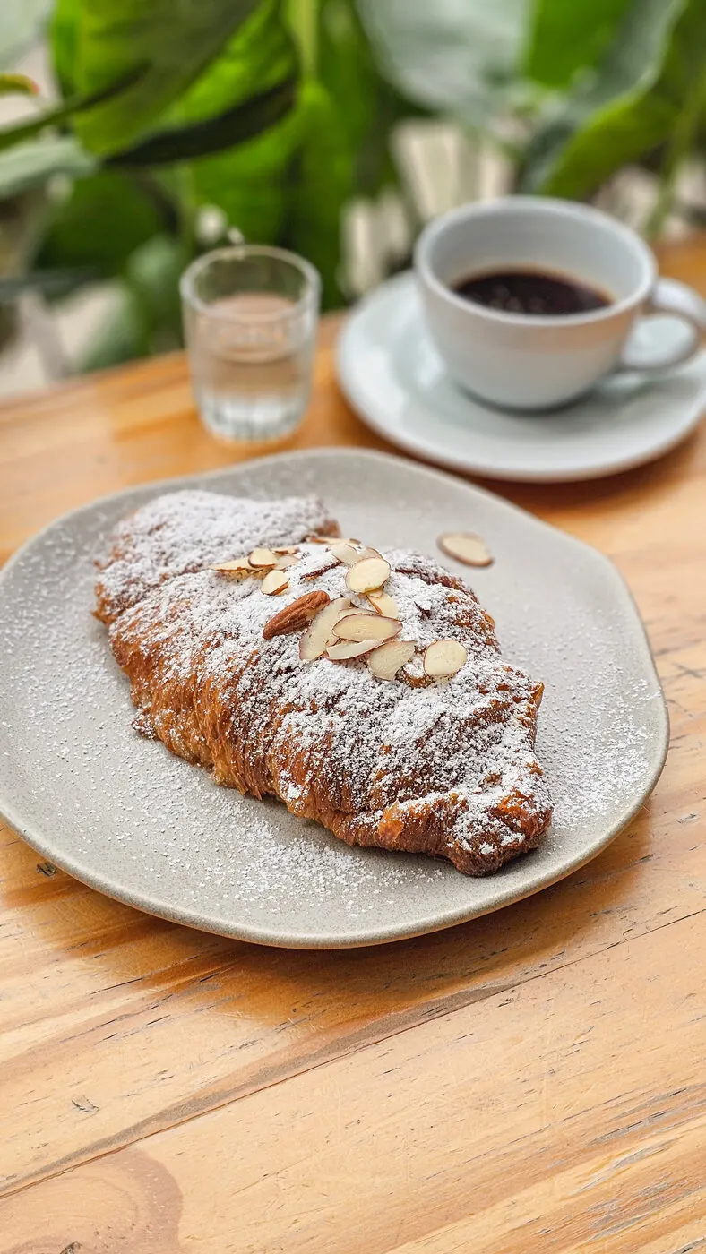 Croissant de almendras con azúcar glas junto a un café
