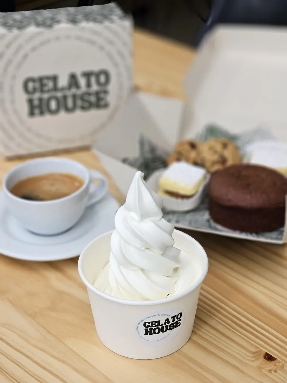 Caja de Gelato House con galletas y postres, junto a un helado de yogurt y un café