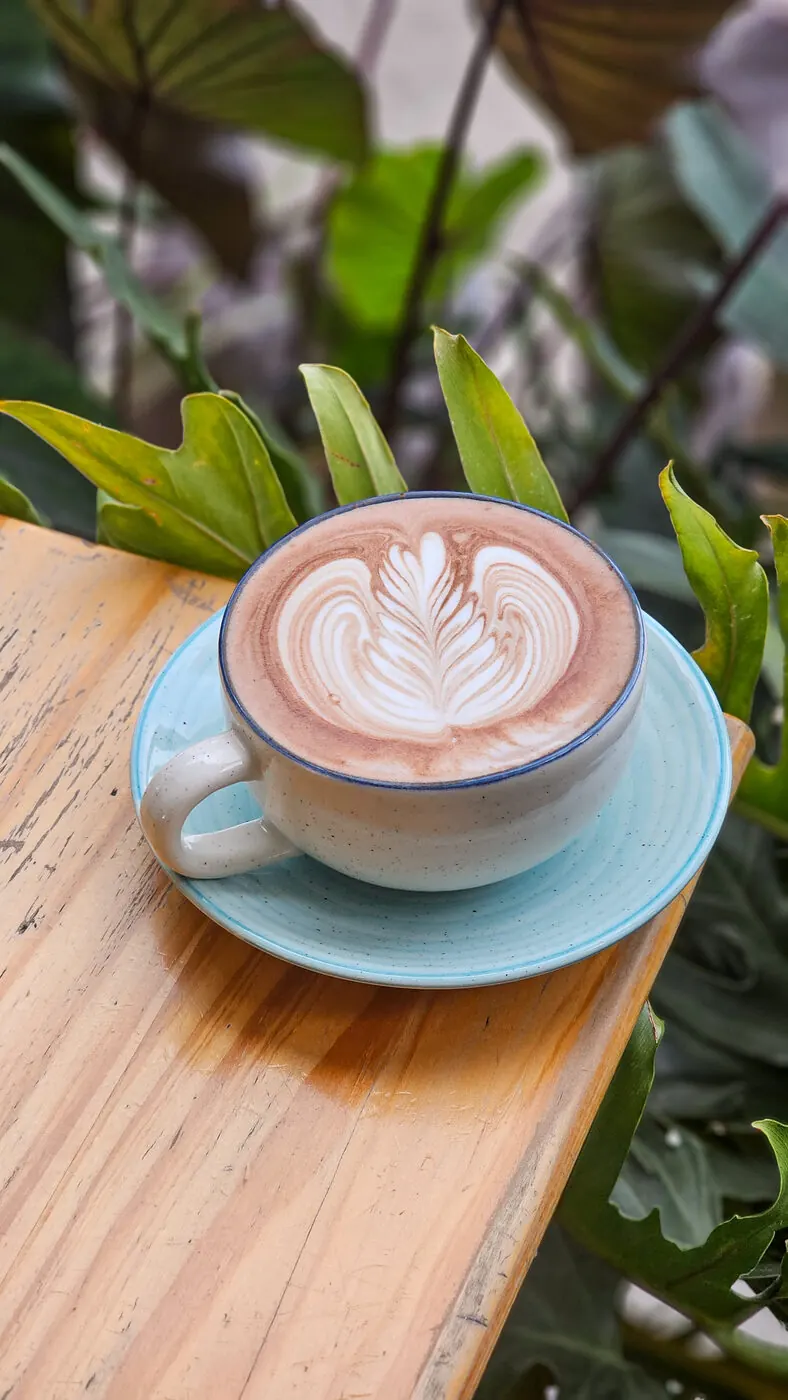 Taza de café con arte latte en forma de hoja, sobre una mesa de madera